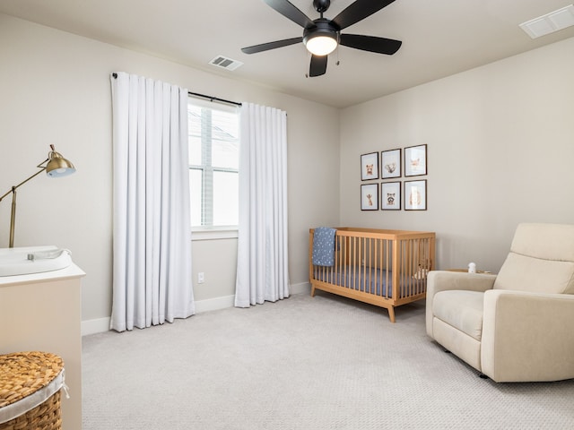 carpeted bedroom with ceiling fan and a nursery area