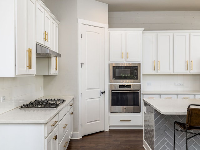 kitchen with dark wood-type flooring, white cabinetry, stainless steel appliances, decorative backsplash, and a breakfast bar