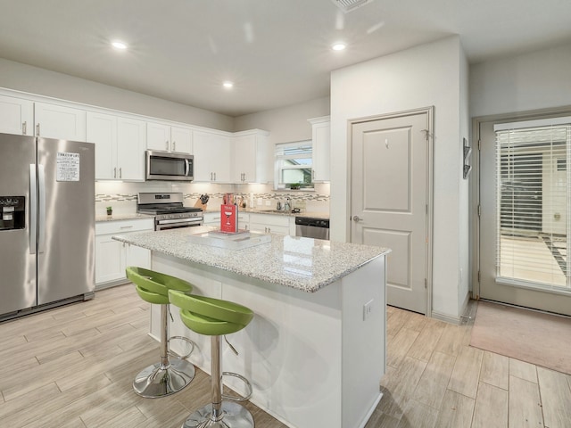 kitchen featuring white cabinets, a center island, light stone countertops, and appliances with stainless steel finishes