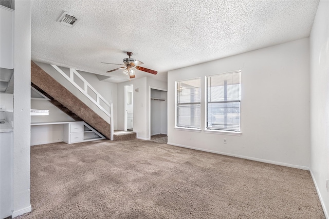 unfurnished living room featuring carpet floors, ceiling fan, a textured ceiling, and built in desk