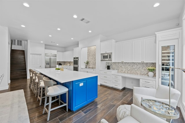 kitchen with built in appliances, a spacious island, white cabinets, a breakfast bar, and backsplash