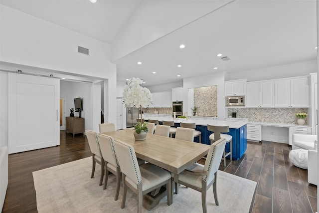 dining space with high vaulted ceiling, dark wood-type flooring, and a barn door