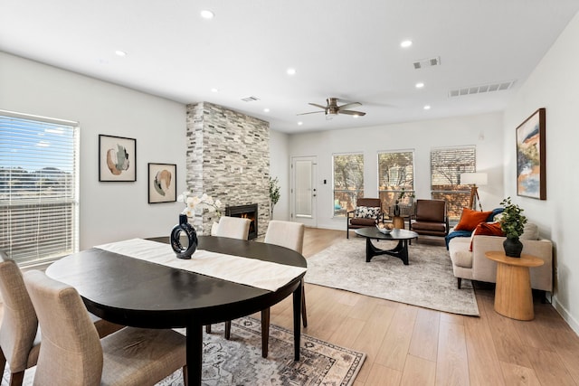 dining room featuring ceiling fan, a stone fireplace, and light hardwood / wood-style flooring