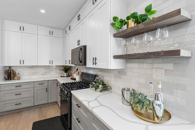 kitchen with tasteful backsplash, light stone counters, black appliances, light hardwood / wood-style floors, and white cabinets