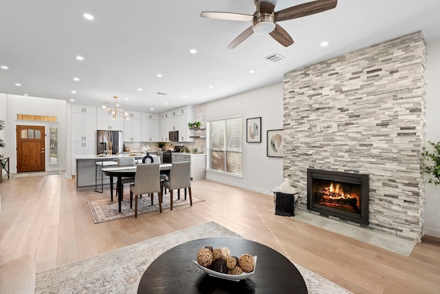 living room featuring ceiling fan, a tiled fireplace, and light hardwood / wood-style flooring