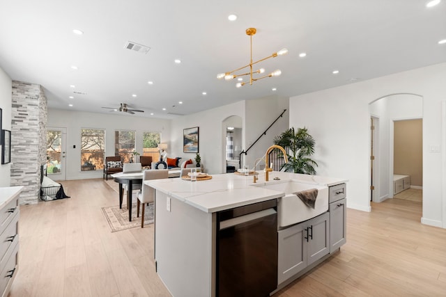 kitchen with dishwashing machine, sink, hanging light fixtures, light hardwood / wood-style floors, and a center island with sink