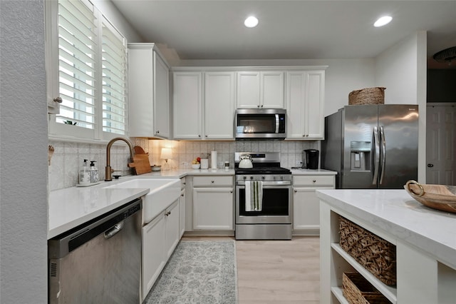 kitchen featuring appliances with stainless steel finishes, tasteful backsplash, sink, white cabinets, and light wood-type flooring