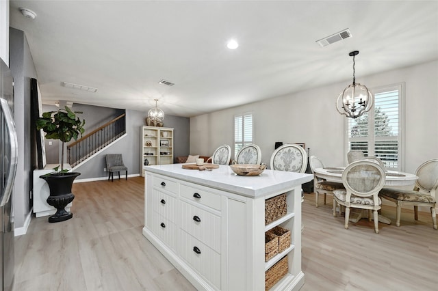 kitchen featuring light hardwood / wood-style flooring, white cabinetry, hanging light fixtures, an inviting chandelier, and a kitchen island