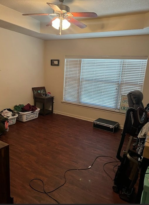 misc room with dark wood-type flooring, a tray ceiling, and ceiling fan