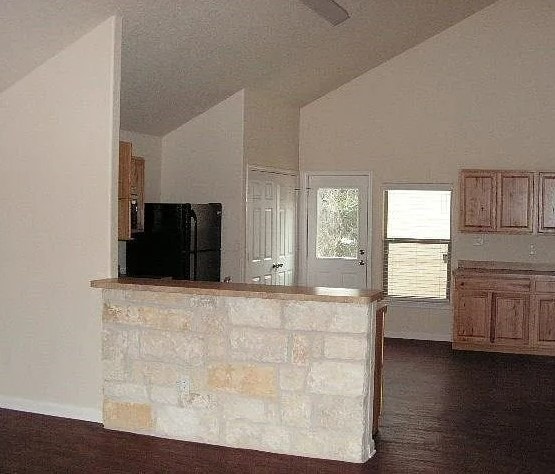 kitchen featuring dark wood-type flooring, black refrigerator, kitchen peninsula, and vaulted ceiling