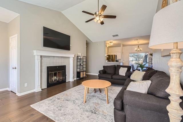 living room with ceiling fan with notable chandelier, dark hardwood / wood-style floors, a tiled fireplace, and vaulted ceiling