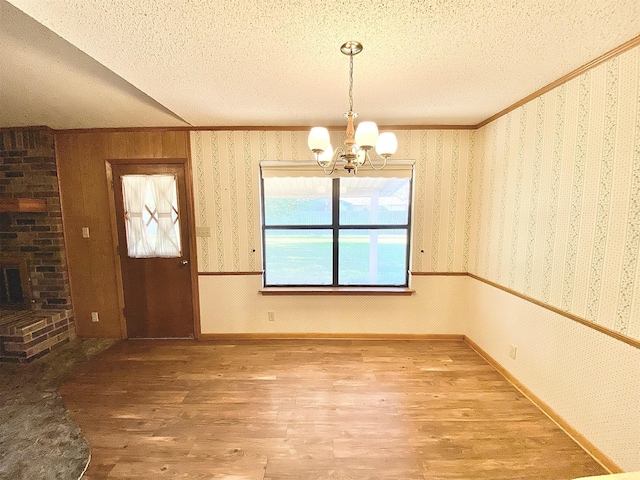 unfurnished dining area featuring a chandelier, a textured ceiling, a fireplace, and wood-type flooring