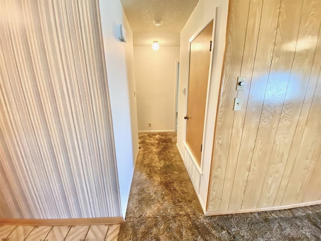 corridor with dark carpet, wooden walls, and a textured ceiling