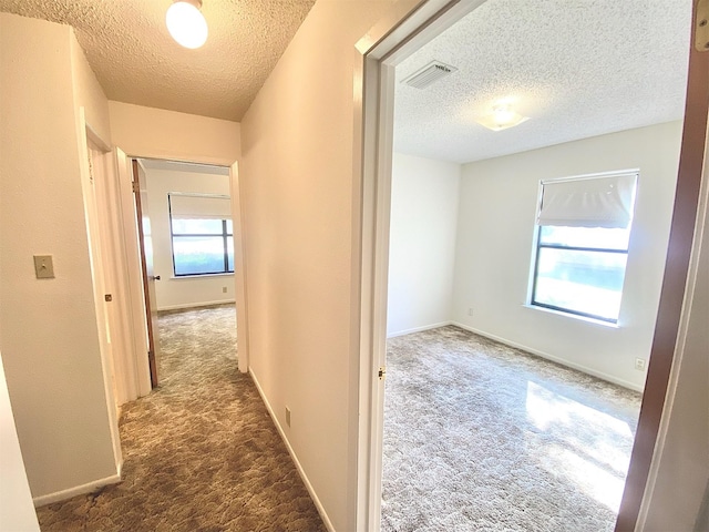 hall featuring dark carpet, a healthy amount of sunlight, and a textured ceiling