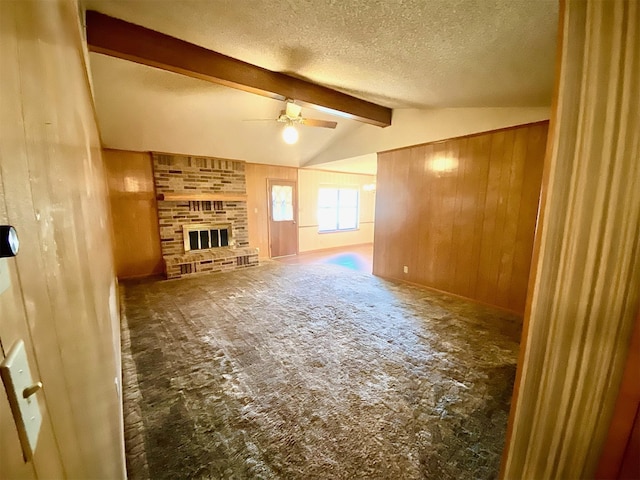 unfurnished living room with a textured ceiling, wooden walls, ceiling fan, lofted ceiling with beams, and a brick fireplace