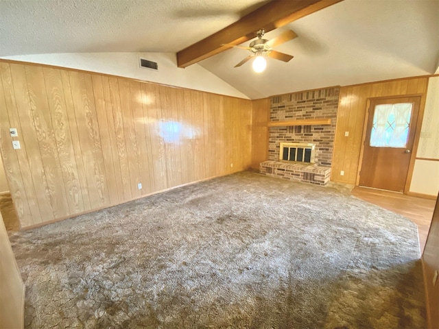 unfurnished living room featuring light carpet, lofted ceiling with beams, a fireplace, a textured ceiling, and wood walls