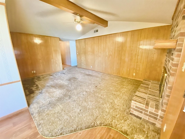 carpeted empty room with ceiling fan, wooden walls, a fireplace, and lofted ceiling with beams