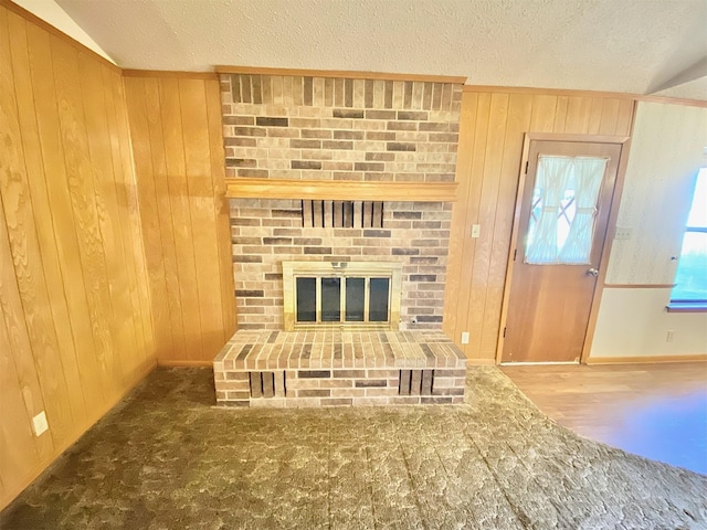 unfurnished living room with wood walls, a textured ceiling, vaulted ceiling, and a brick fireplace