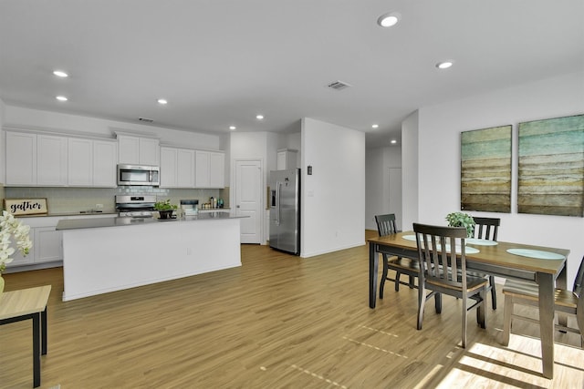 kitchen featuring appliances with stainless steel finishes, tasteful backsplash, white cabinetry, a kitchen island with sink, and light wood-type flooring