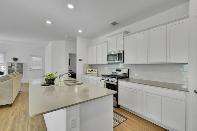 kitchen featuring stainless steel appliances, white cabinetry, sink, and a center island with sink