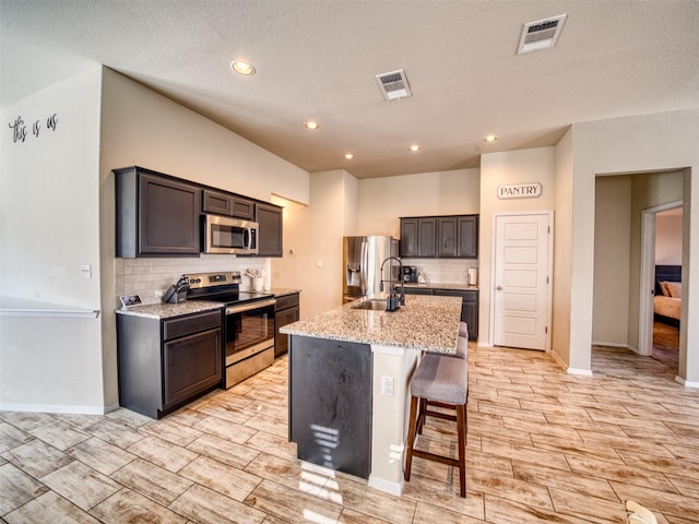 kitchen featuring light stone countertops, a kitchen bar, stainless steel appliances, sink, and a center island with sink