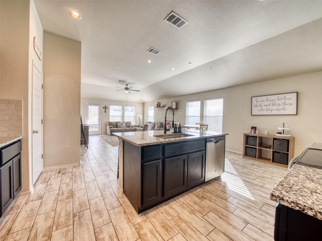 kitchen with dishwasher, sink, light stone countertops, a healthy amount of sunlight, and a center island with sink