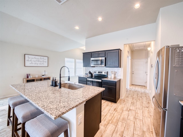 kitchen featuring sink, a center island with sink, light stone counters, and appliances with stainless steel finishes