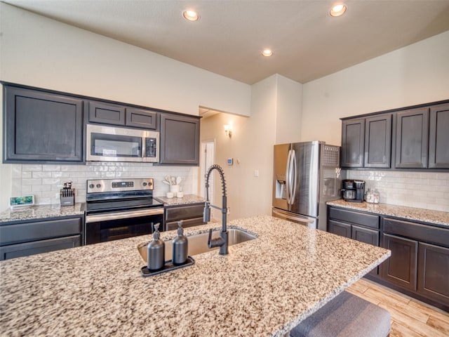 kitchen featuring light stone counters, backsplash, light hardwood / wood-style flooring, and appliances with stainless steel finishes