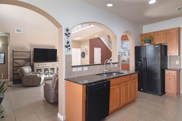 kitchen featuring black appliances, dark stone counters, light tile patterned floors, and sink