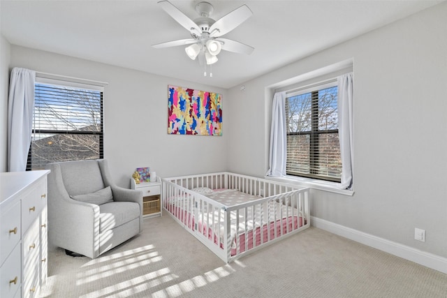 carpeted bedroom featuring ceiling fan and a nursery area