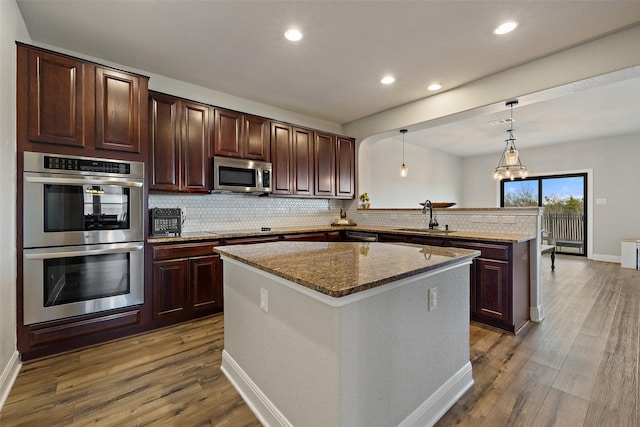 kitchen with kitchen peninsula, hanging light fixtures, sink, a kitchen island, and stainless steel appliances