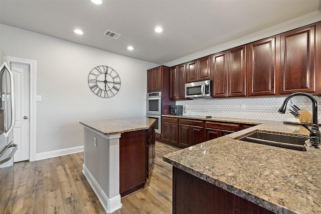 kitchen with sink, light wood-type flooring, a center island, decorative backsplash, and stainless steel appliances