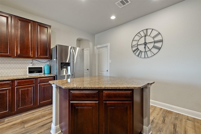 kitchen featuring light stone countertops, a center island, light hardwood / wood-style floors, backsplash, and stainless steel fridge with ice dispenser