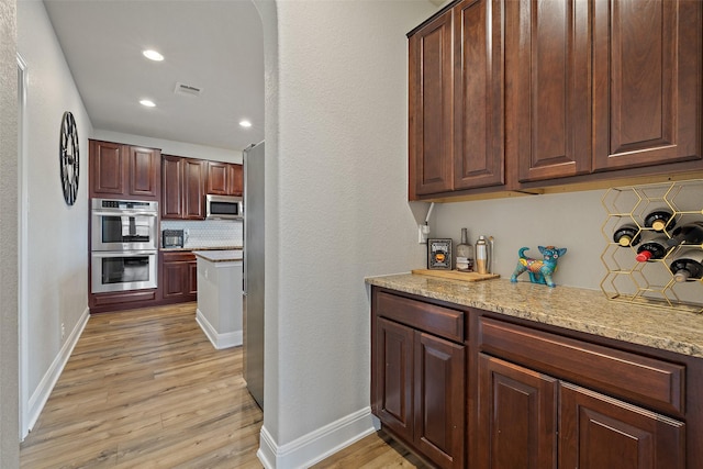 kitchen featuring light stone counters, light hardwood / wood-style flooring, appliances with stainless steel finishes, and tasteful backsplash