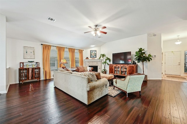 living room with vaulted ceiling, a stone fireplace, dark wood-type flooring, and visible vents