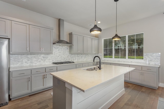 kitchen with wall chimney range hood, sink, gray cabinets, hanging light fixtures, and stainless steel appliances