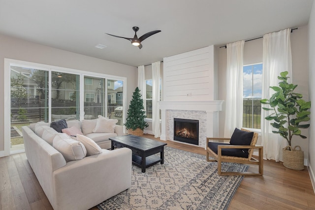 living room featuring ceiling fan, a tiled fireplace, and light wood-type flooring