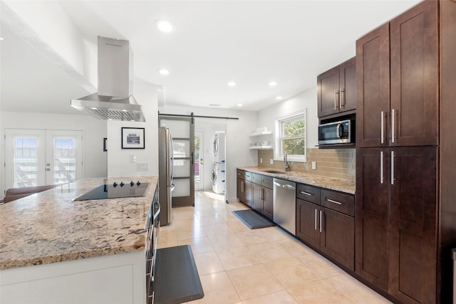 kitchen with stacked washer / drying machine, tasteful backsplash, ventilation hood, stainless steel appliances, and a barn door