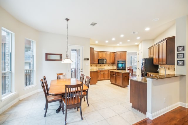 kitchen with pendant lighting, black appliances, decorative backsplash, dark stone counters, and kitchen peninsula