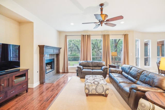 living room with a wealth of natural light, light hardwood / wood-style flooring, a premium fireplace, and ceiling fan