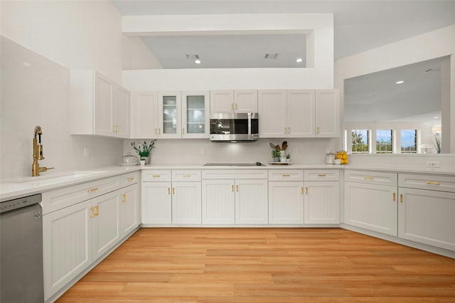 kitchen featuring sink, light wood-type flooring, appliances with stainless steel finishes, beam ceiling, and white cabinets