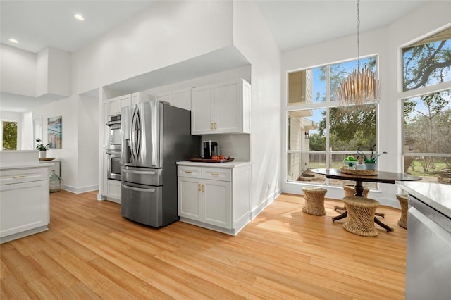 kitchen with a healthy amount of sunlight, a high ceiling, light wood-style floors, and stainless steel appliances