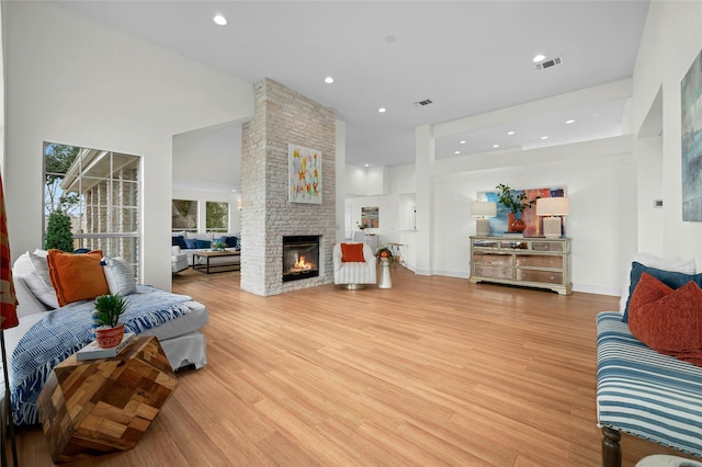 living room with a towering ceiling, a fireplace, and light hardwood / wood-style flooring