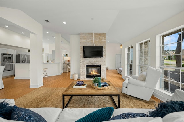 living room featuring a fireplace, vaulted ceiling, and light wood-type flooring