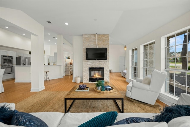 living room with visible vents, recessed lighting, a fireplace, vaulted ceiling, and light wood-style floors