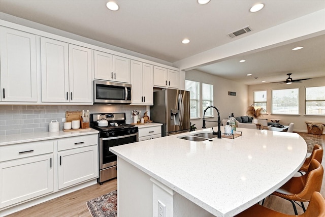 kitchen featuring tasteful backsplash, a center island with sink, white cabinets, and appliances with stainless steel finishes