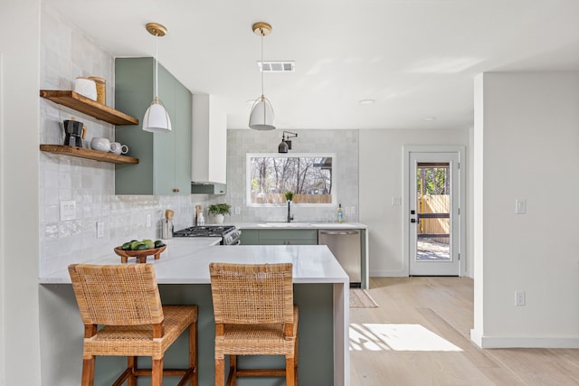 kitchen featuring a breakfast bar area, appliances with stainless steel finishes, tasteful backsplash, kitchen peninsula, and light wood-type flooring