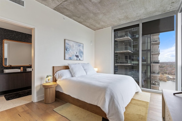 bedroom with sink, light hardwood / wood-style flooring, and a wall of windows