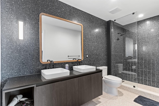 bathroom with a tile shower, tile walls, vanity, and toilet