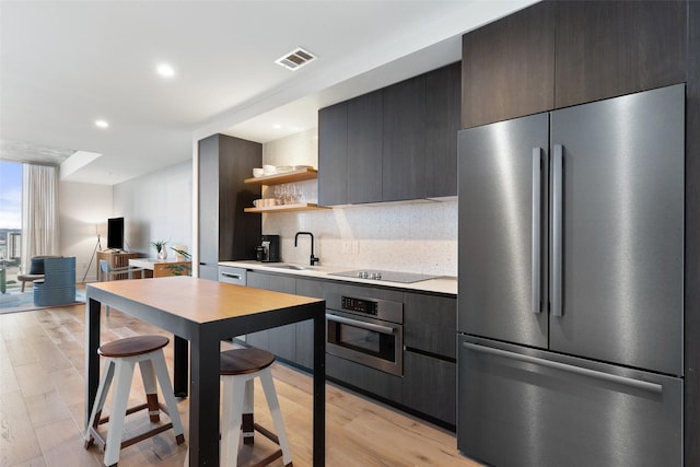 kitchen featuring tasteful backsplash, stainless steel appliances, sink, and light hardwood / wood-style flooring